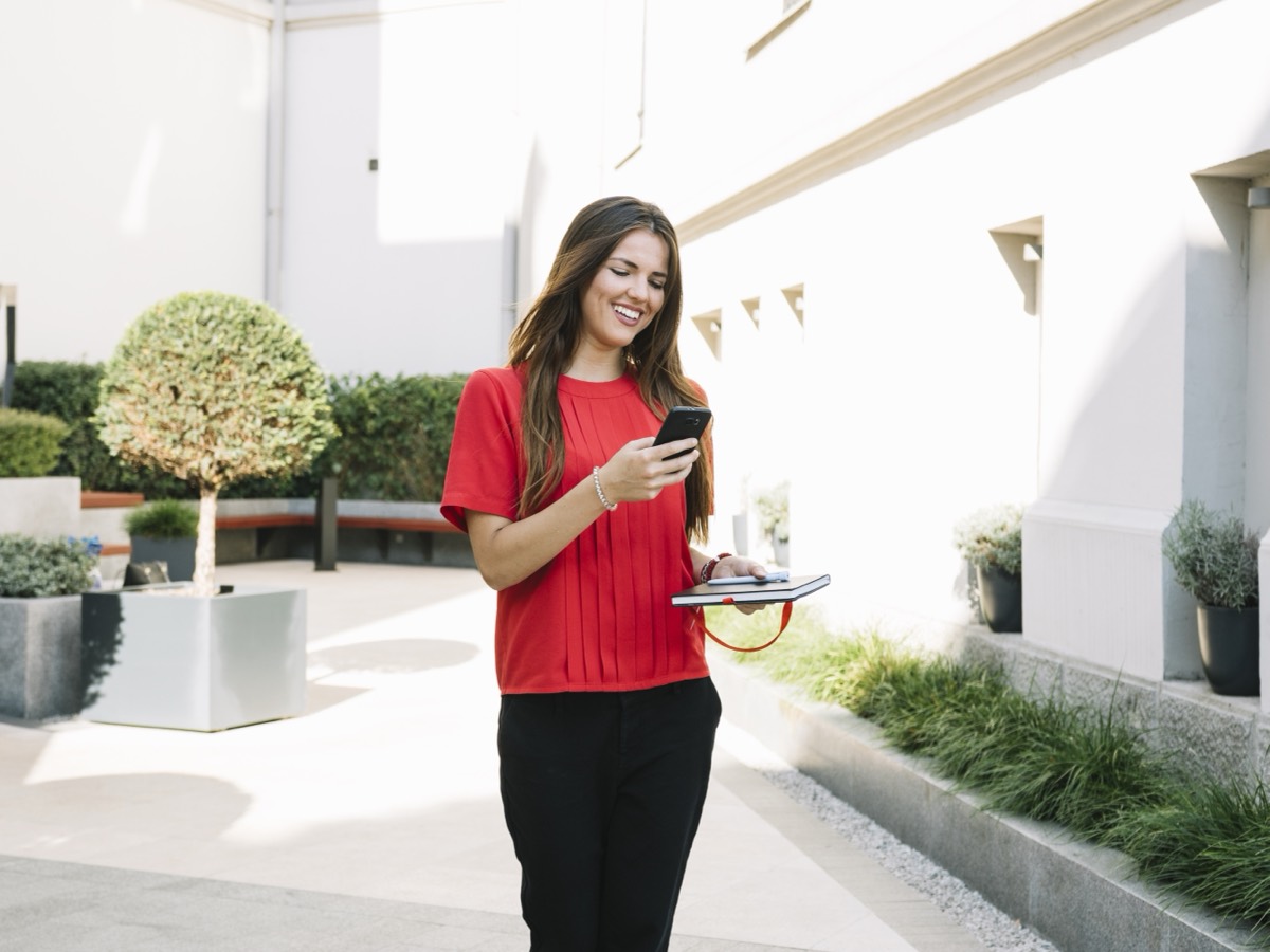 A real estate agent replying to a lead on her phone beside a for-sale sign